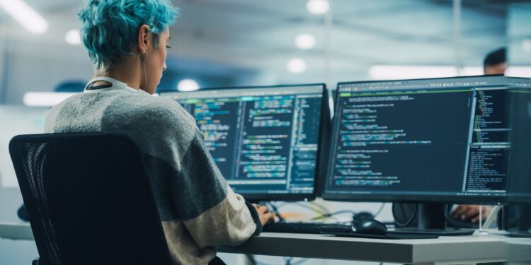 In Diverse Office: Young Stylish Woman in Working on Desktop Computer. Colorful Haired Girl Digital Entrepreneur Creating Modern Software, e-Commerce App Design, e-Business Coding. Over Shoulder Shot
